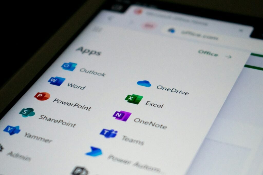 Angled white phone screen shows colorful "Apps" icons: "Outlook," "Word," "PowerPoint," "Excel," "OneDrive," and "Teams."